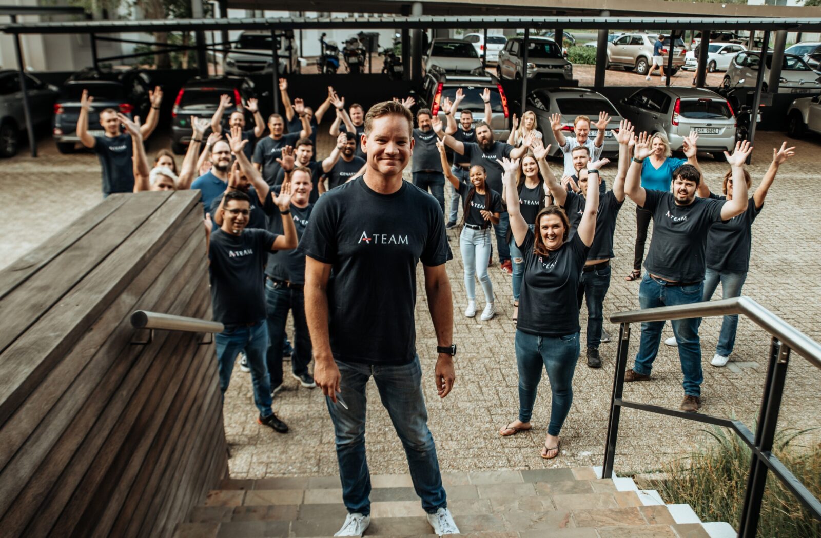 Genasys Cape Town team waving outside the new Product and Innovation Campus in A-Team T-shirts