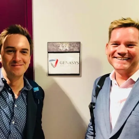 Two colleagues standing beside a Genasys office door sign