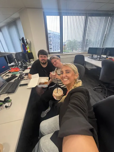 Three colleagues with iced coffees and brownies at their desks