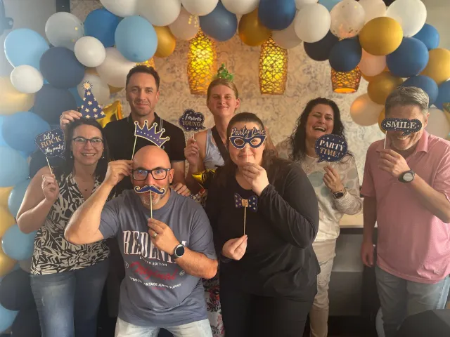 Colleagues posing with photo-booth props in front of balloons