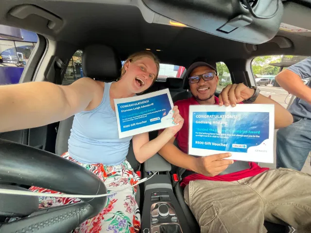 Two colleagues holding up award certificates in a car