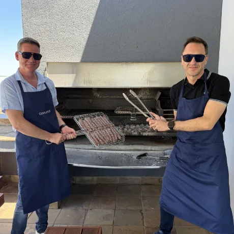 Two colleagues in Genasys aprons grilling at a braai