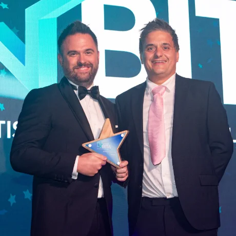 Two colleagues on stage at the BITA Awards, one holding a trophy