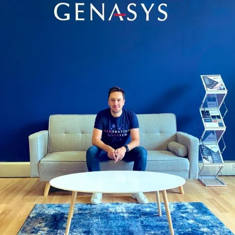 A colleague sitting on a sofa under the Genasys sign