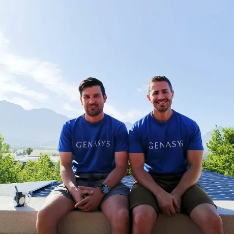 Two colleagues in Genasys t-shirts on a rooftop with mountains behind them