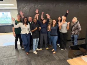 Ten colleagues in the office with their hands in the air, one in an A-Team shirt
